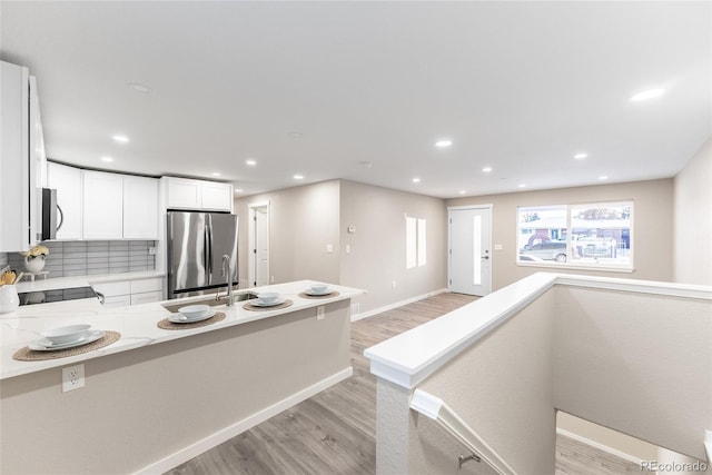 kitchen with light stone counters, backsplash, appliances with stainless steel finishes, light wood-style floors, and white cabinetry