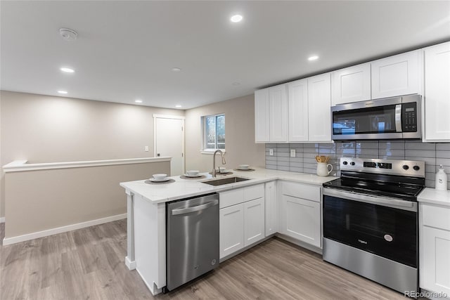 kitchen featuring stainless steel appliances, a peninsula, a sink, and white cabinets