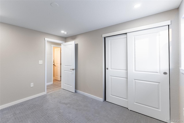 unfurnished bedroom with recessed lighting, baseboards, a closet, and light colored carpet