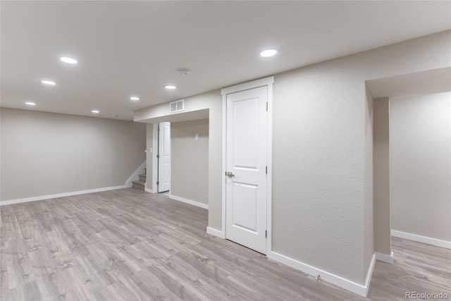 finished below grade area featuring light wood-type flooring, stairway, baseboards, and visible vents