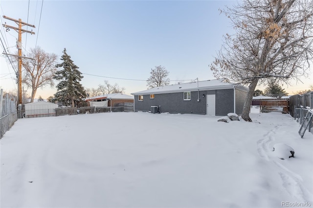 snow covered rear of property featuring a fenced backyard and central air condition unit