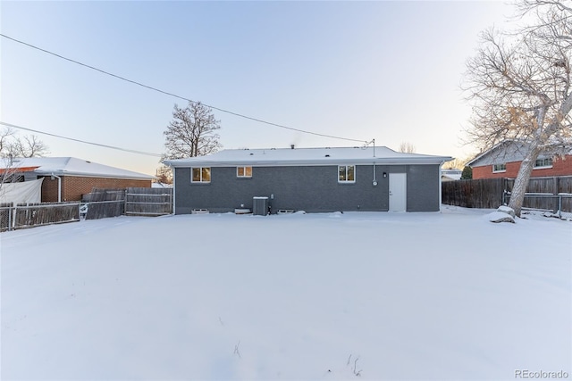 snow covered house featuring central AC unit and a fenced backyard