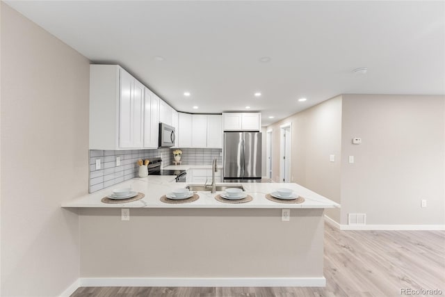 kitchen with appliances with stainless steel finishes, white cabinetry, a sink, and a peninsula