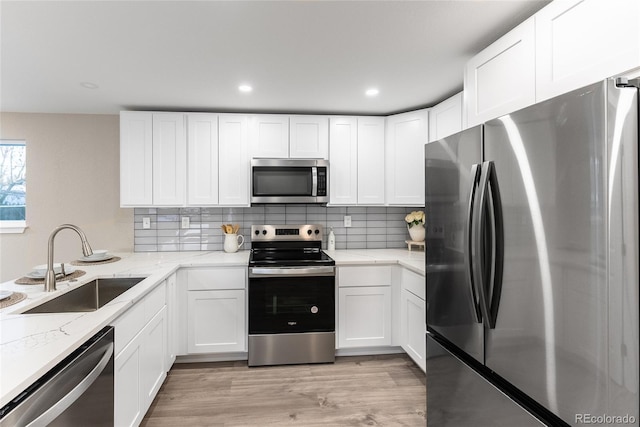 kitchen with stainless steel appliances, white cabinets, a sink, and light stone counters