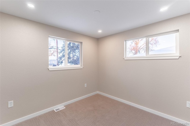 carpeted empty room with a healthy amount of sunlight, visible vents, and baseboards