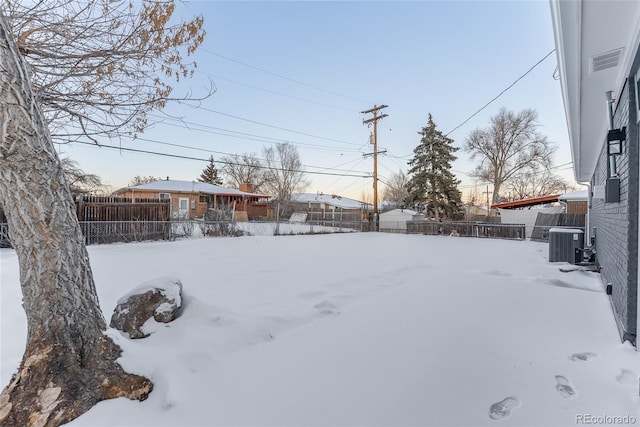 snowy yard featuring central AC and fence