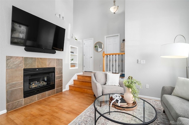 living room featuring wood-type flooring, a tiled fireplace, and built in features