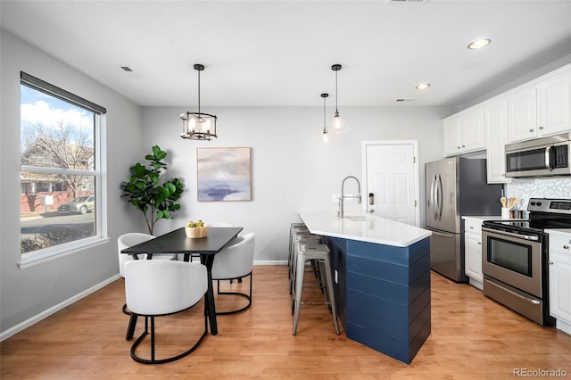 kitchen with light hardwood / wood-style flooring, stainless steel appliances, white cabinets, a center island with sink, and decorative light fixtures