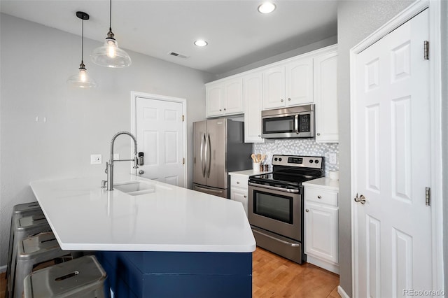 kitchen with appliances with stainless steel finishes, decorative light fixtures, tasteful backsplash, sink, and white cabinets