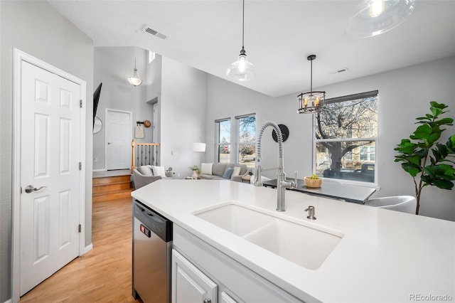 kitchen featuring decorative light fixtures, sink, white cabinets, stainless steel dishwasher, and light wood-type flooring