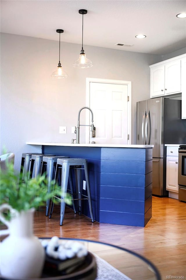 kitchen featuring white cabinetry, sink, hanging light fixtures, stainless steel appliances, and light wood-type flooring