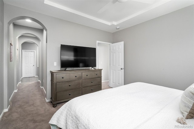 carpeted bedroom with a raised ceiling and ceiling fan