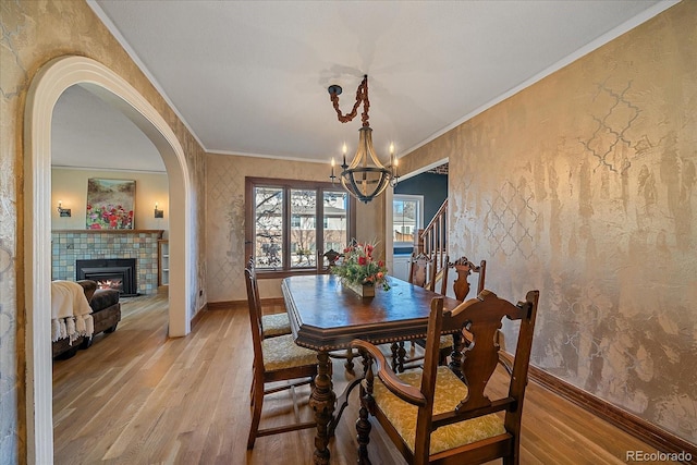 dining area featuring a fireplace, an inviting chandelier, light hardwood / wood-style flooring, and crown molding