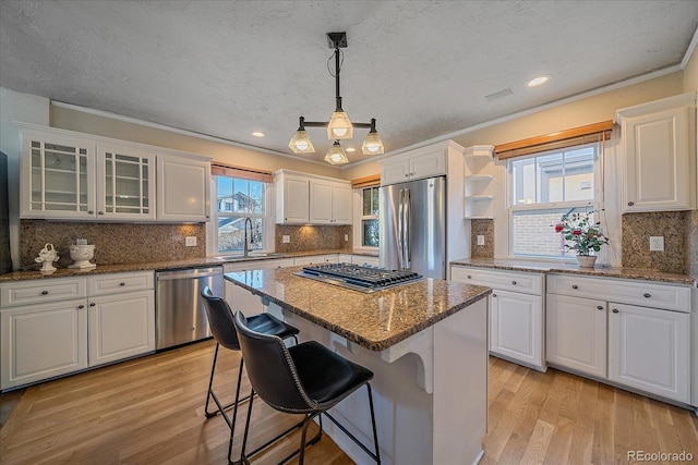 kitchen with white cabinets, stainless steel appliances, a kitchen island, and hanging light fixtures