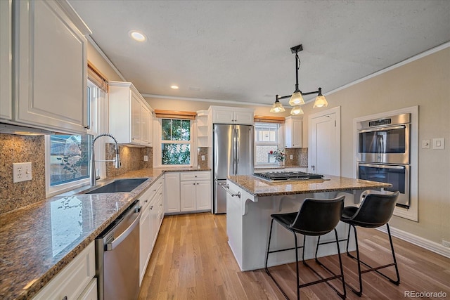 kitchen with stainless steel appliances, sink, decorative light fixtures, a center island, and white cabinetry