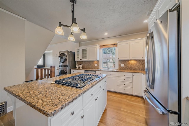 kitchen featuring appliances with stainless steel finishes, stacked washing maching and dryer, a center island, white cabinetry, and hanging light fixtures