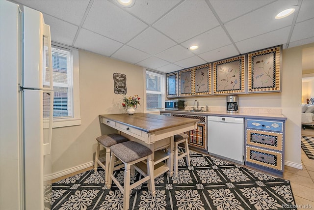 kitchen with tile patterned flooring, a drop ceiling, white appliances, and sink