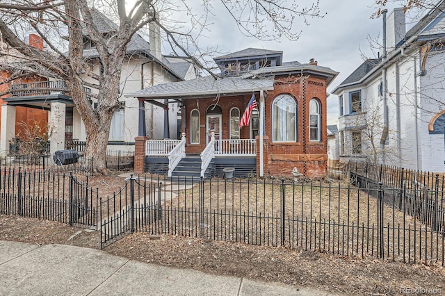 view of front of property featuring a fenced front yard, covered porch, a shingled roof, and brick siding