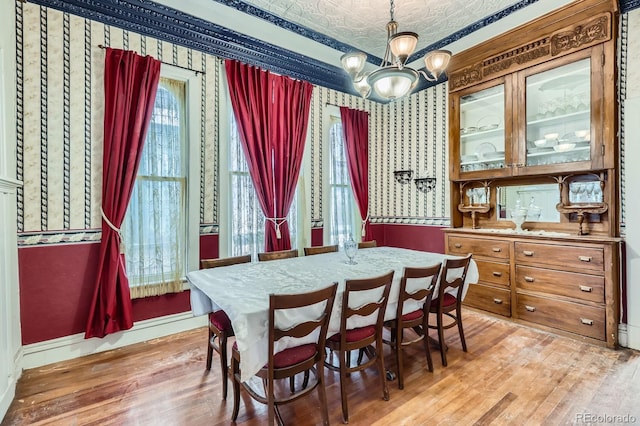 dining area with an ornate ceiling, an inviting chandelier, light wood-style flooring, and wallpapered walls