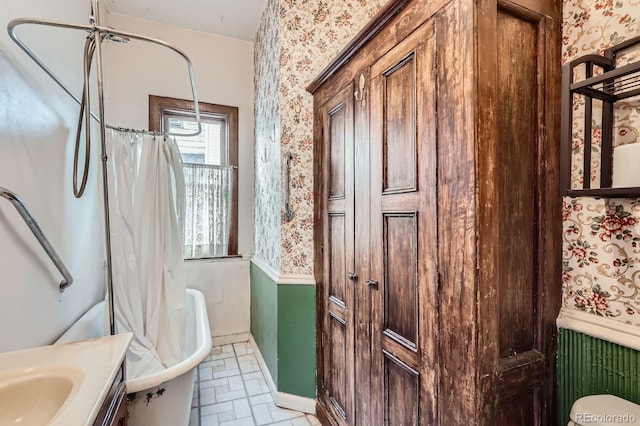 bathroom featuring a wainscoted wall, brick patterned floor, wallpapered walls, and a tub to relax in