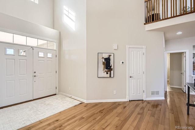 foyer featuring visible vents, a high ceiling, light wood-type flooring, and baseboards