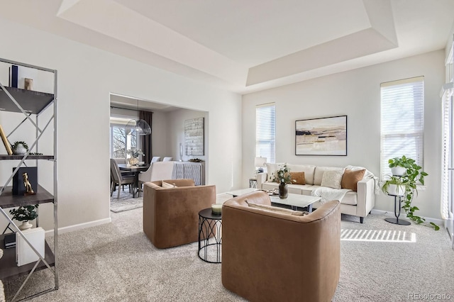 living room with carpet flooring, a tray ceiling, plenty of natural light, and baseboards