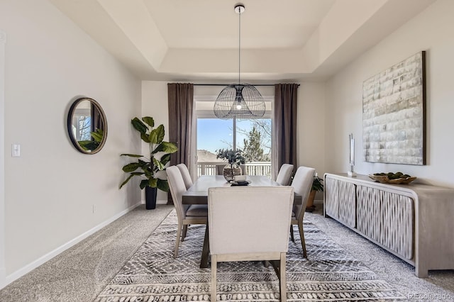 dining room featuring light colored carpet, a raised ceiling, and baseboards