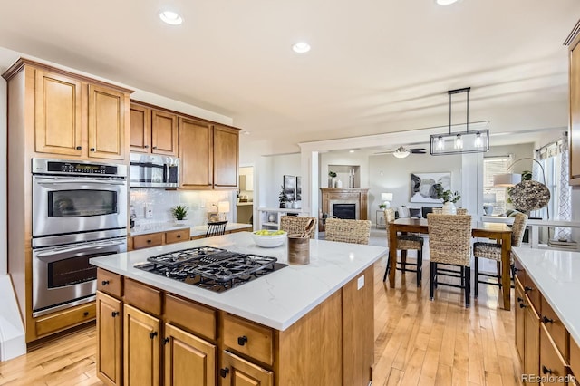 kitchen with backsplash, a kitchen island, stainless steel appliances, light wood-style floors, and a fireplace