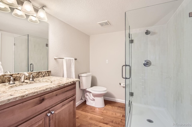 bathroom featuring vanity, wood finished floors, visible vents, a shower stall, and a textured ceiling