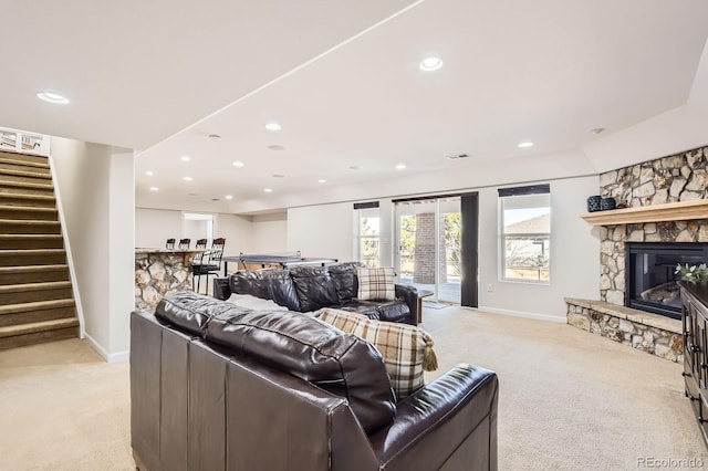 living area featuring recessed lighting, a stone fireplace, light colored carpet, and stairs