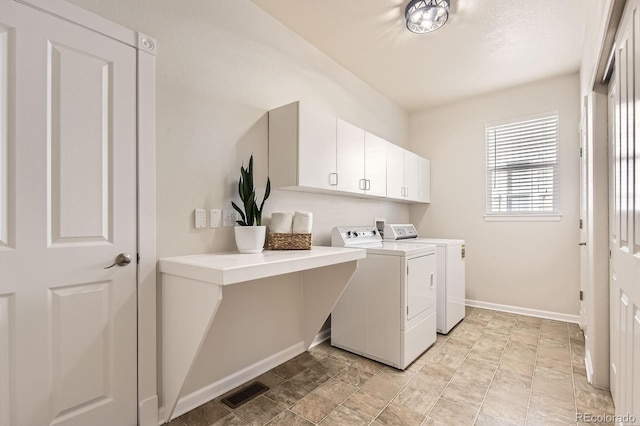 clothes washing area featuring washing machine and clothes dryer, visible vents, cabinet space, and baseboards