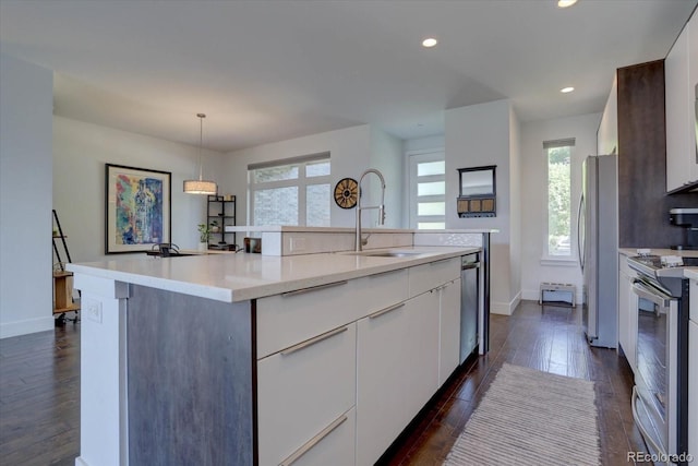 kitchen with appliances with stainless steel finishes, white cabinetry, a wealth of natural light, and an island with sink