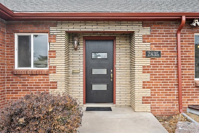 doorway to property featuring roof with shingles and brick siding