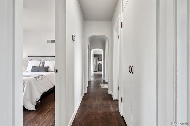 hallway featuring arched walkways, dark wood-style flooring, visible vents, and baseboards