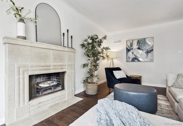 living room featuring baseboards, a fireplace, visible vents, and wood finished floors