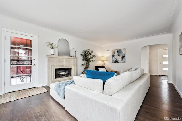 living area featuring arched walkways, a fireplace, visible vents, baseboards, and dark wood finished floors