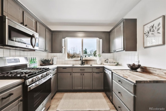 kitchen with appliances with stainless steel finishes, a sink, light wood finished floors, and decorative backsplash