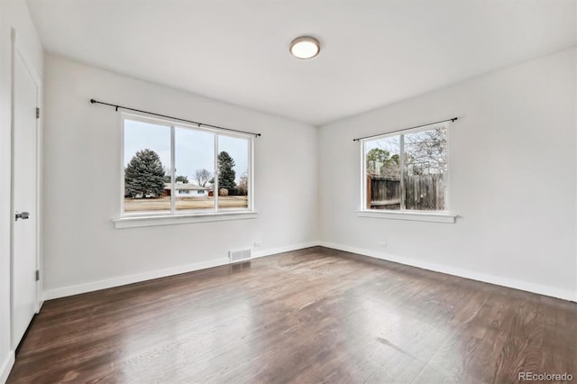 empty room with wood finished floors, visible vents, and baseboards