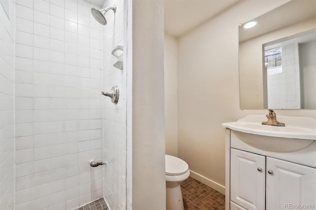 full bath featuring toilet, a tile shower, vanity, and baseboards