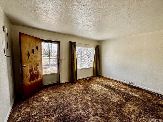 spare room with a textured wall, dark colored carpet, visible vents, and baseboards