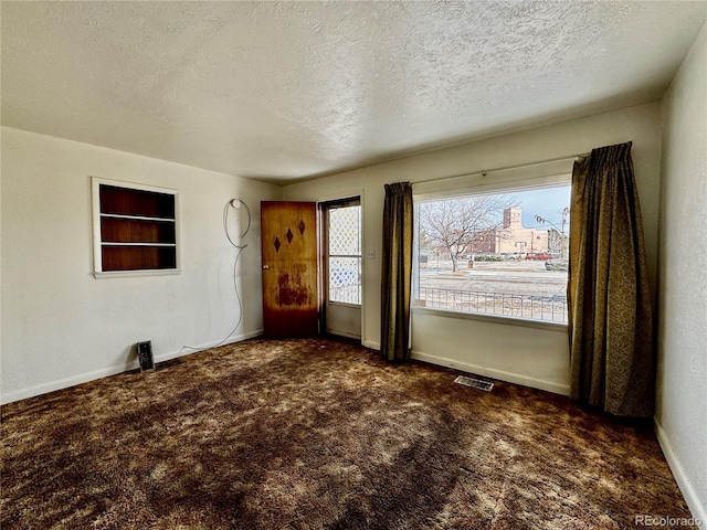 interior space with a textured ceiling, dark carpet, visible vents, and baseboards