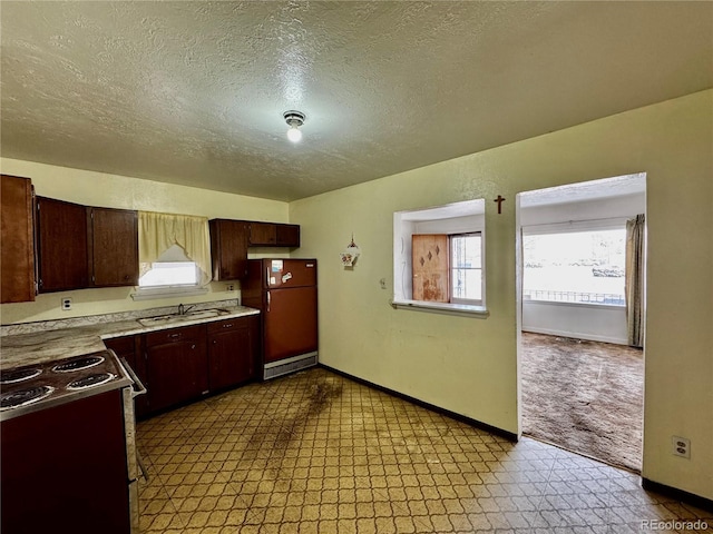 kitchen with electric range oven, refrigerator, light countertops, light floors, and a sink