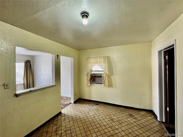 spare room featuring a textured wall, cooling unit, visible vents, baseboards, and tile patterned floors