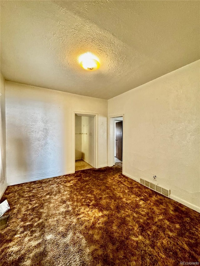 empty room with carpet floors, visible vents, a textured ceiling, and a textured wall