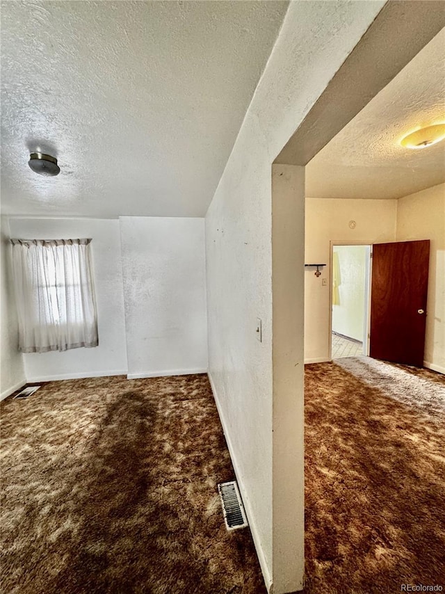 interior space with a textured ceiling, visible vents, and baseboards