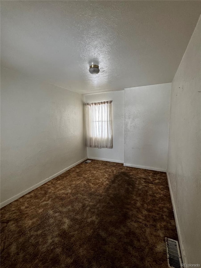 empty room featuring a textured ceiling, a textured wall, carpet flooring, visible vents, and baseboards