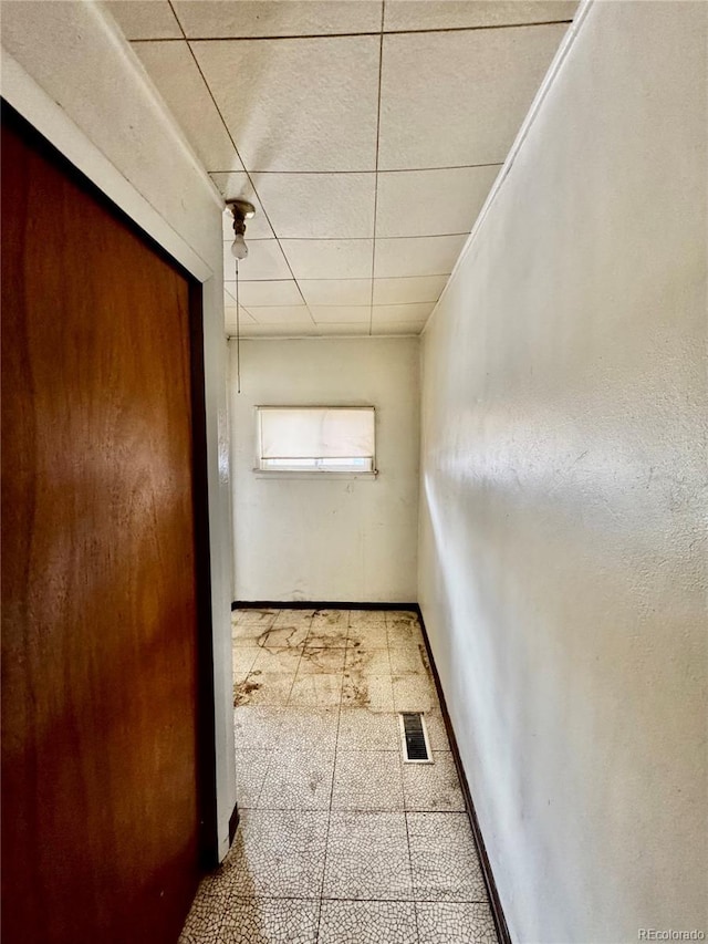 hall with light floors, a drop ceiling, visible vents, and baseboards