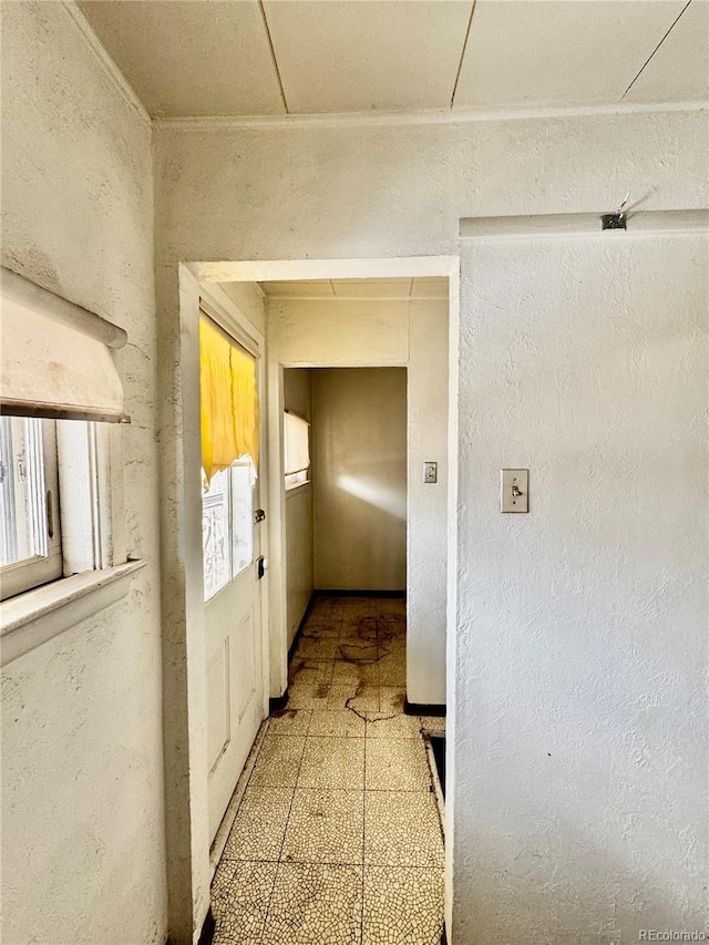 hallway featuring light floors, ornamental molding, and a textured wall