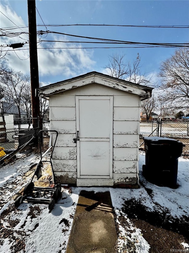 snow covered structure with an outbuilding, a shed, and fence