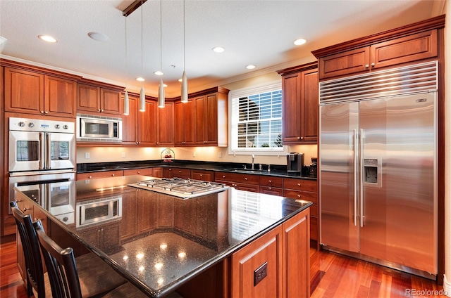 kitchen featuring dark stone counters, built in appliances, a kitchen island, light wood-type flooring, and decorative light fixtures